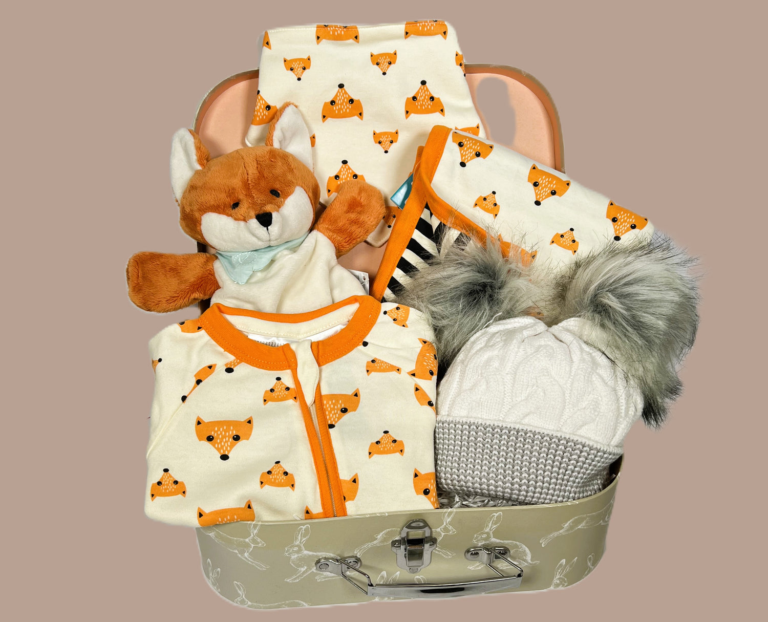 Baby hamper containing a cotton fox print zipped baby sleepsuit and matching dribble bib. A fox print baby blanket. A Kaloo fox baby comforter and puppet. A grey and white baby pompom hat in a sage green baby keepsake case.