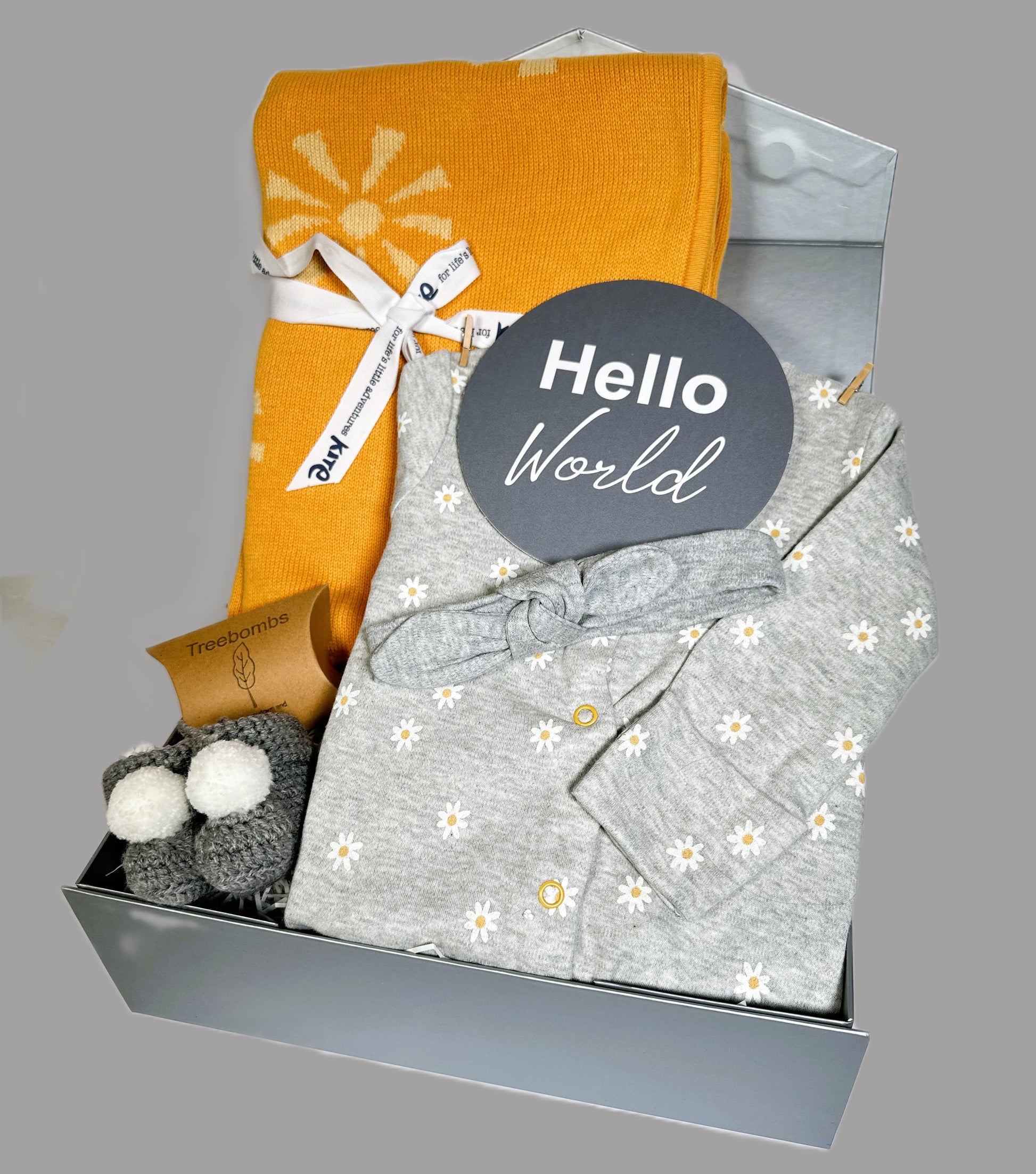New baby girl hamper gift box containing a cotton baby sleepsuit with a white and yellow daisy print and a cotton baby headband. An Organic cotton baby blanket with a sunshine print.