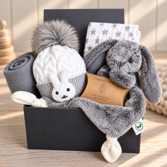 a curated grey and white new baby gift with Mary Meyer bunny baby comforter, baby hat, baby muslin and a bigger grey baby muslin with white pompom fringing, in a grey baby keepsake box.
