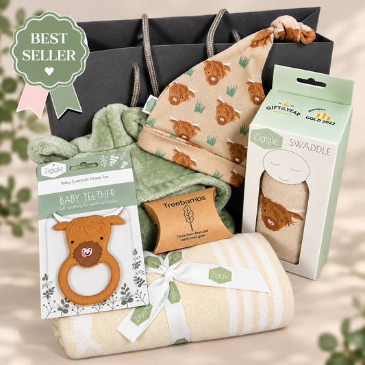 A baby gift set arranged in front of a grey gift bag, including a cream and white striped baby blanket tied with a white ribbon, a silicone highland cow teething ring in packaging, a green plush hooded baby robe, a beige baby knotty hat with a brown  highland cow print, and a boxed 'Ziggle  highland cow print swaddle'. A green 'Best Seller' badge appears in the top left.