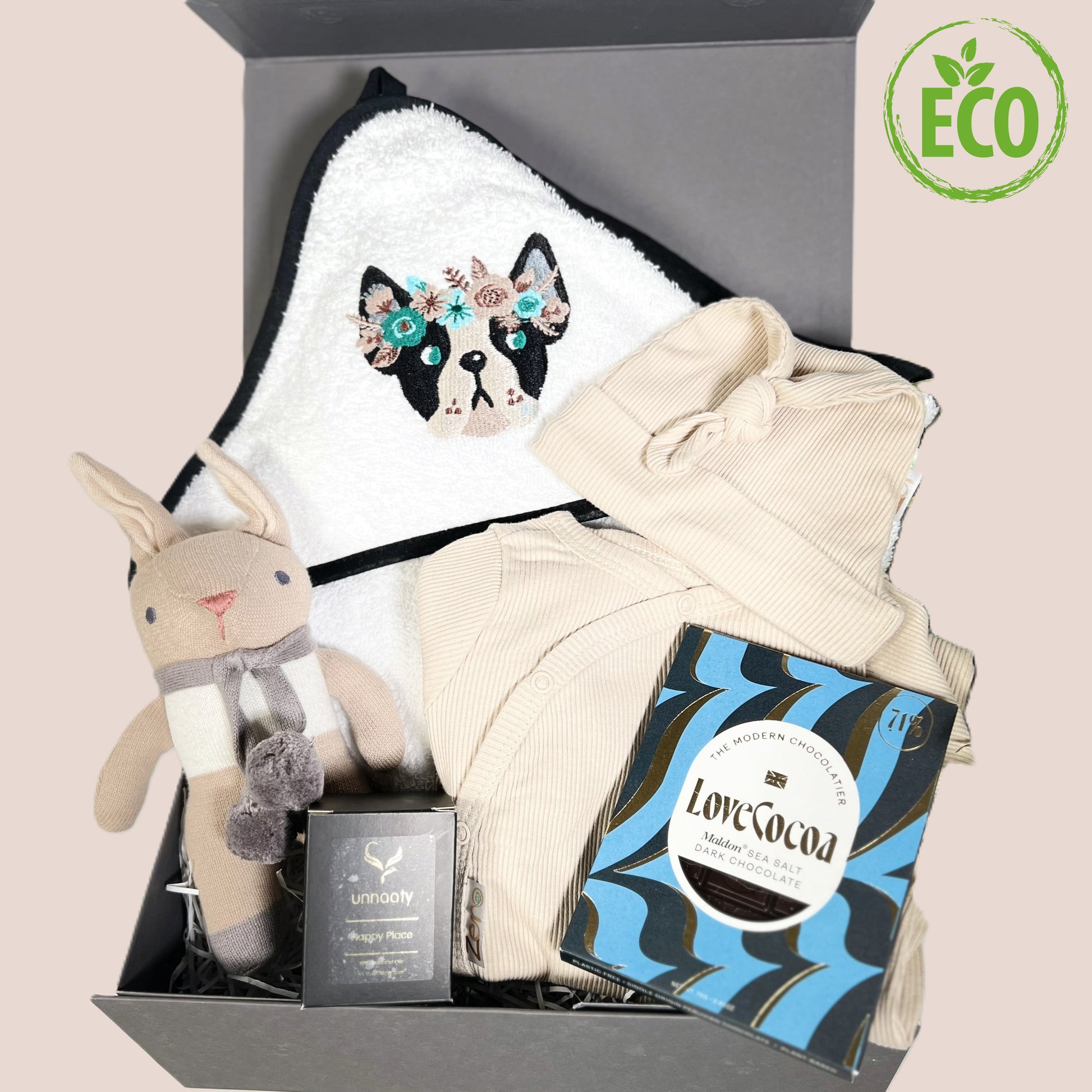 Baby girl hamper with hoded embroidered French bulldog baby towel, cotton sleepsuit in biscuit with matching baby knot hat, essentail oils candle, a n organic cotton bunny baby rattleand a bar of salted caramel Love Cocoa chocolate.