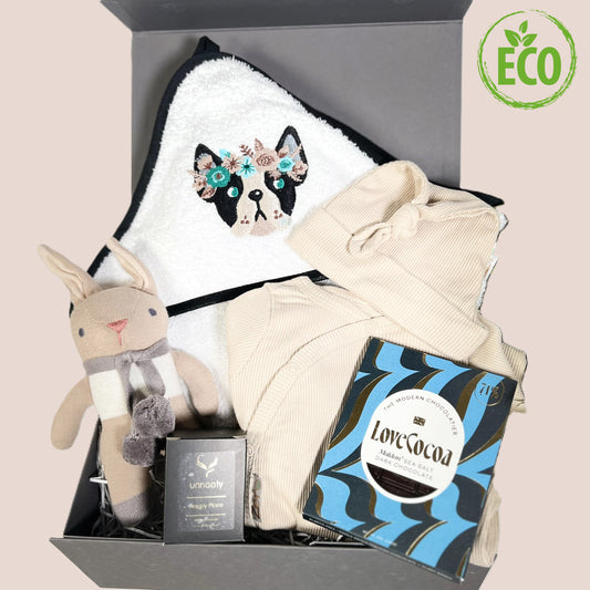 Baby girl hamper with hoded embroidered French bulldog baby towel, cotton sleepsuit in biscuit with matching baby knot hat, essentail oils candle, a n organic cotton bunny baby rattleand a bar of salted caramel Love Cocoa chocolate.