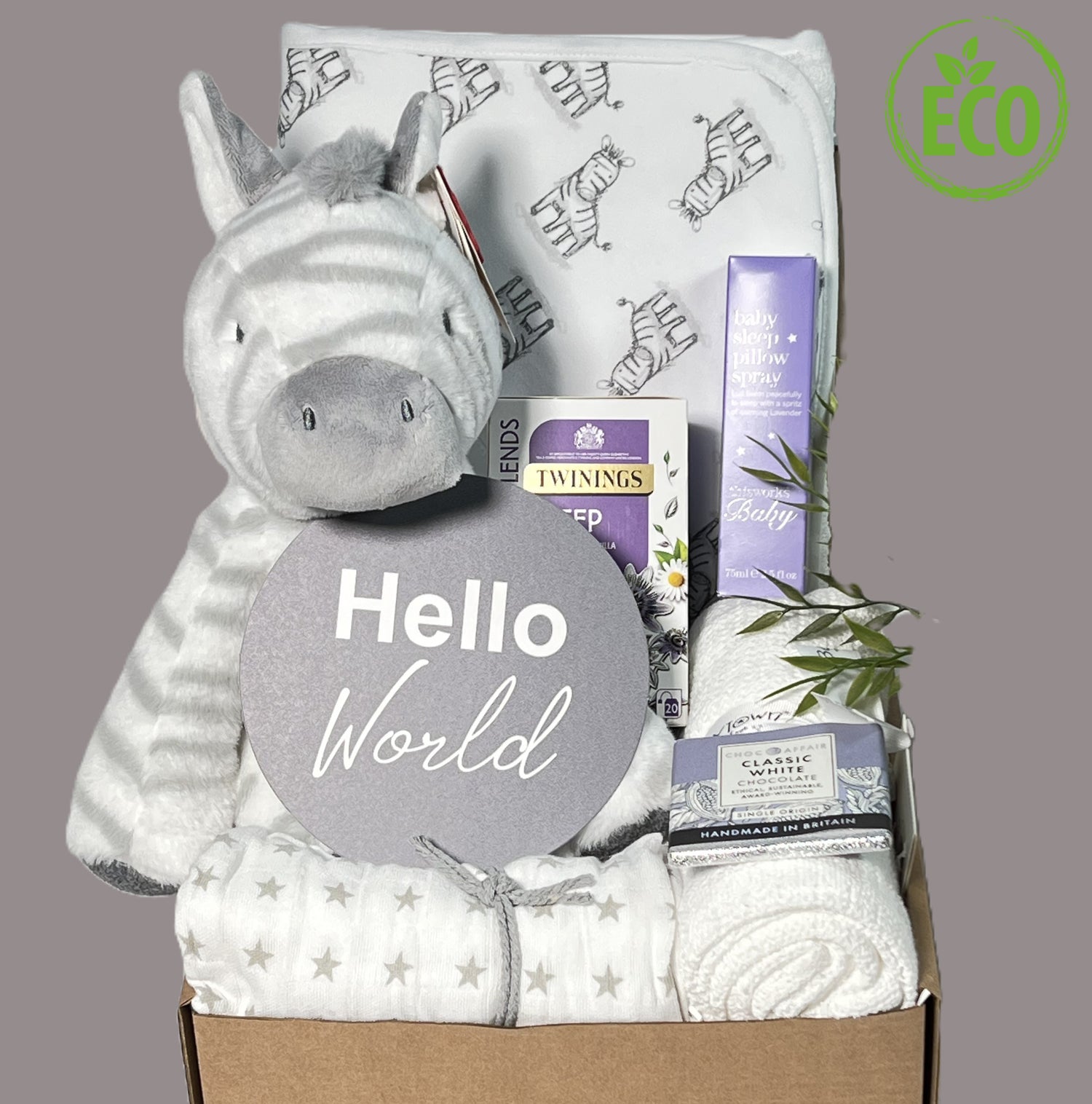 Unisex eco friendly new baby hamper containing a zebra print hooded baby towel, a zebra soft baby toy, a white cellular baby blanket, a bottle of "This Works" baby pillow spray, a packet of Twining "Sleep" teabags and a bar of chocolate.