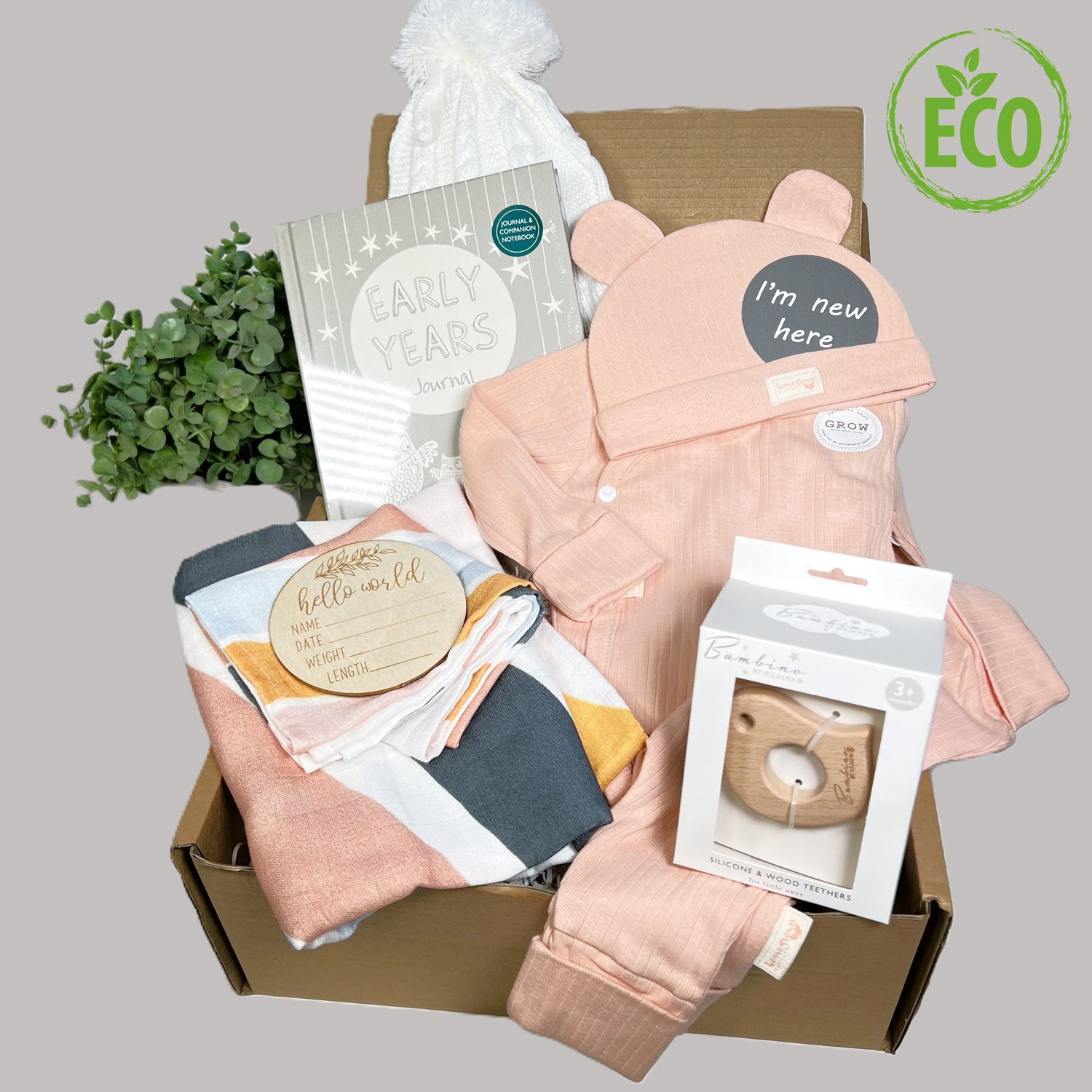 New baby girl gift hamper full of eco friendly new baby essentials to include prganic cotton rainbow swaddle blankets and muslin square, organic cotton peach layette set, Bambino bird teether, baby pompom hat and an early years baby journal.