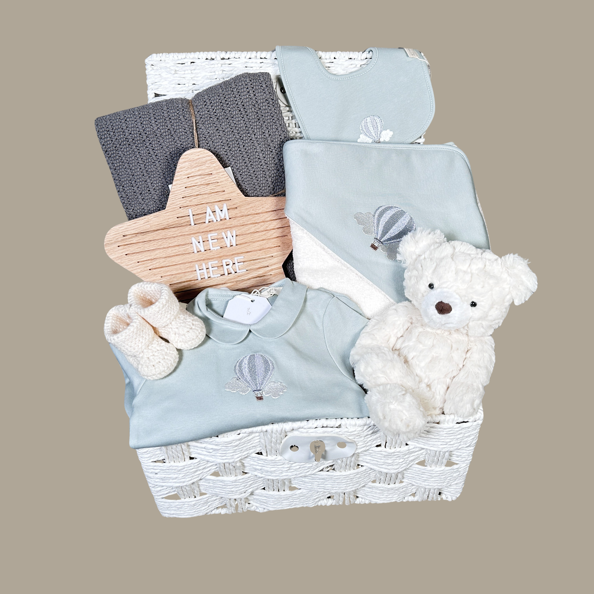 luxury baby hamper in a white paper rope hamper , with sage green baby clothing, hooded baby towel, baby blanket and baby booties
