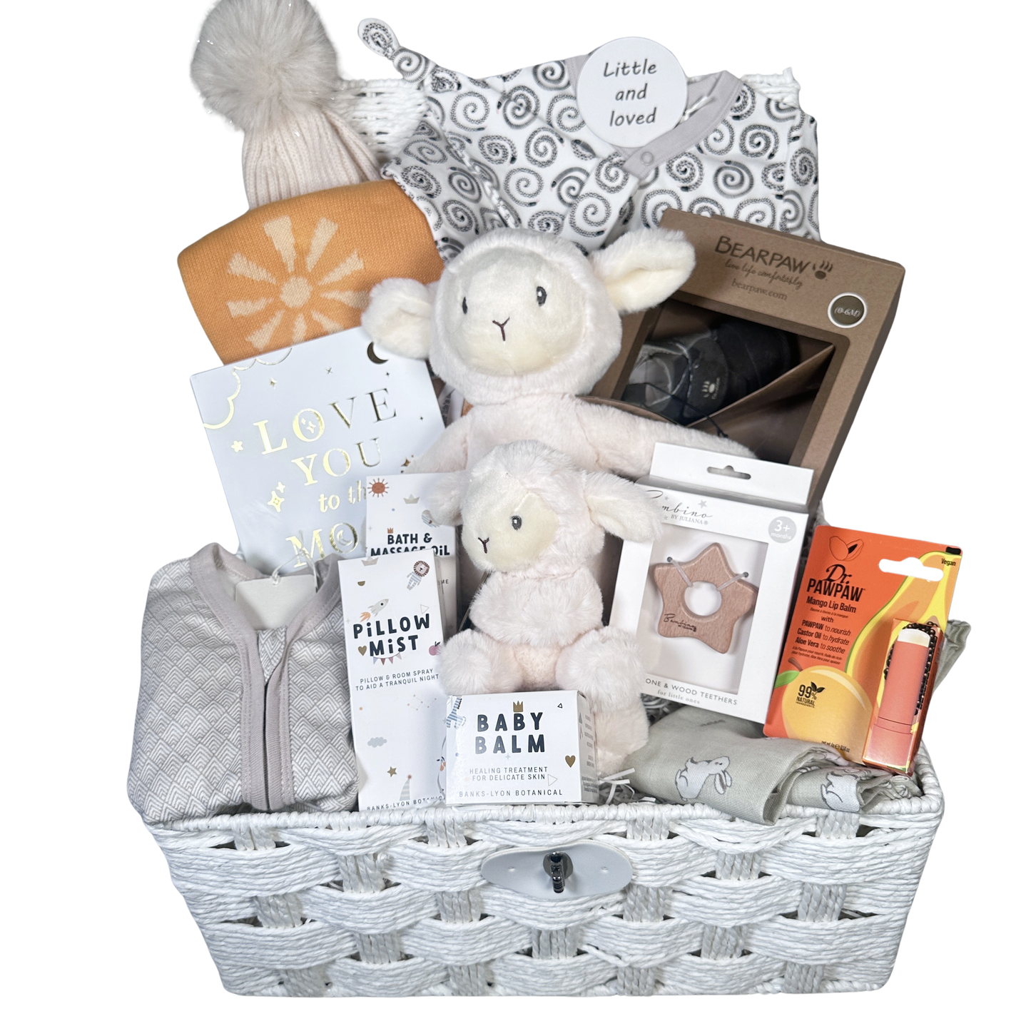 A new baby gift basket filled with baby items including a plush lamb toys, a knit hat with pom-pom, a baby blanket,  arranged in a white wicker basket on a white background.