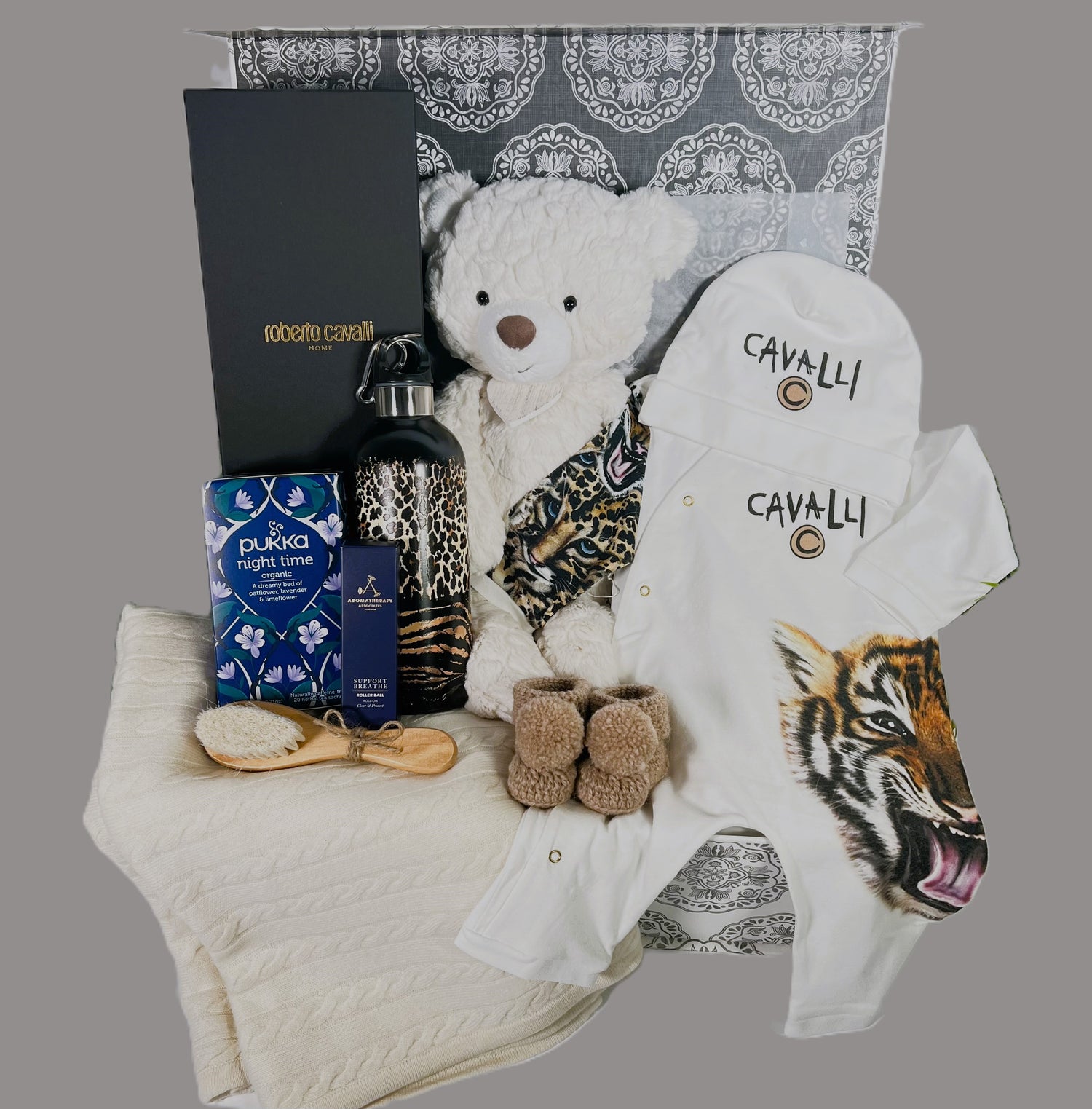 Luxury new parents gift in a baby keepsake box, a Roberto cavelli Tiger baby romper ans matching baby hat, a Roberto Cavelli wtaer bottle, a wooden baby hair brush and comb st, a cream cashmere baby blanket, a pair of merino wool baby booties.