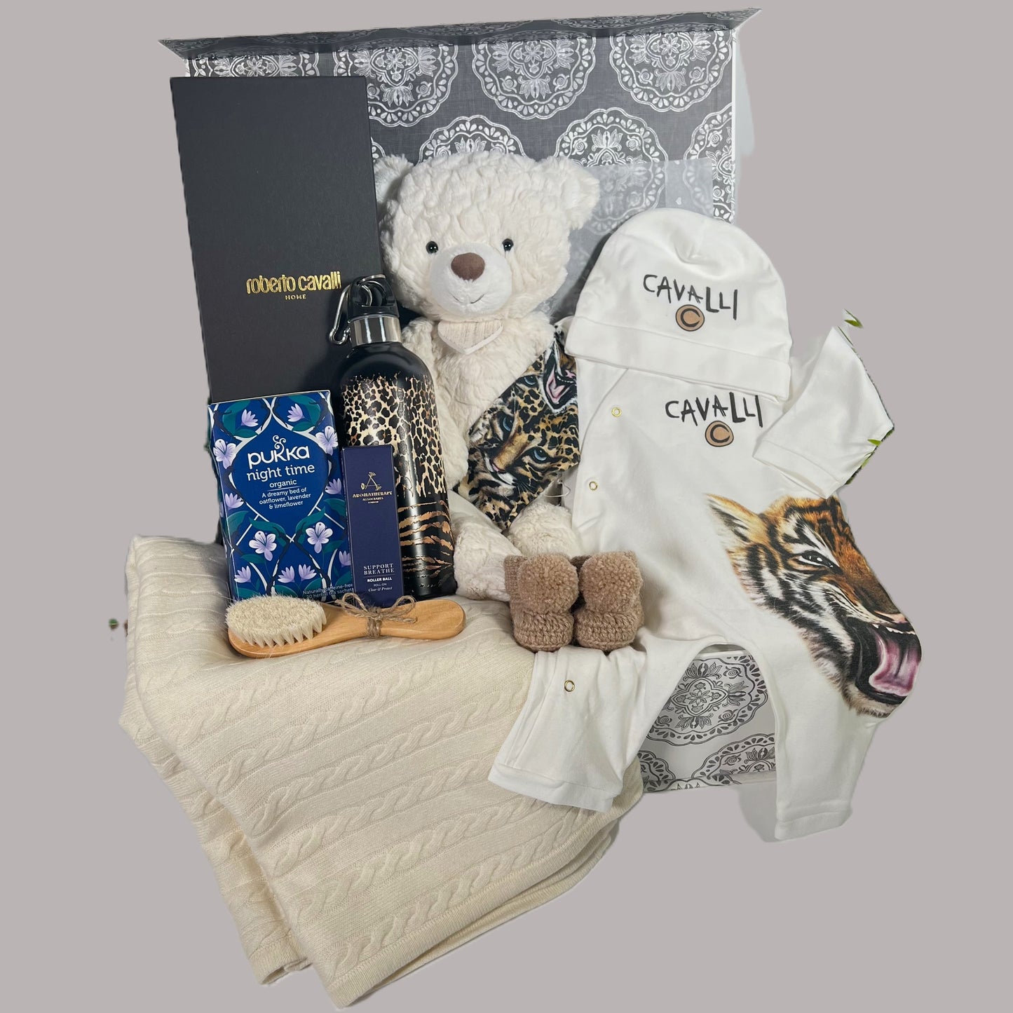 Luxury new parents gift in a baby keepsake box, a Roberto cavelli Tiger baby romper  ans matching baby hat, a Roberto Cavelli wtaer bottle, a wooden baby hair brush and comb st, a cream cashmere baby blanket, a pair of merino wool baby booties.