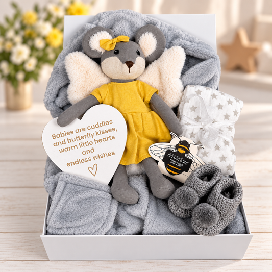 A baby gift box set containing a plush grey mouse toy with white angel wings and a yellow dress, a soft grey baby robe, a white star-patterned baby muslin, a pair of grey crocheted baby booties, and a heart-shaped nursery plaque that reads 'Babies are cuddles and butterfly kisses, warm little hearts and endless wishes'. Bee seedsticks