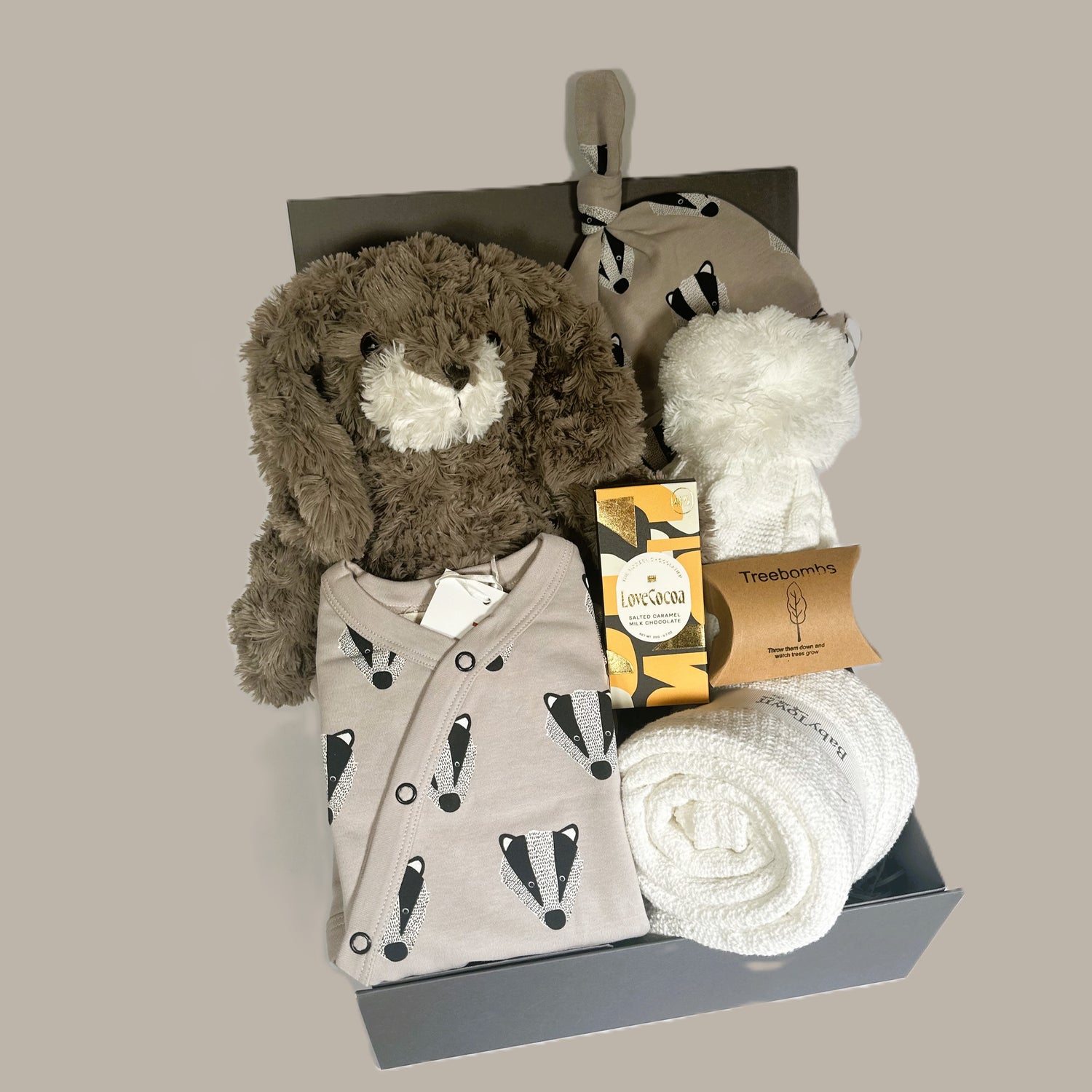 NEW BABY GIF IN A BABY KEEPSAKE BOX WITH A BADGER PRINT BABY ROMPER AND MATCHING HAT. WHITE COTTON CELLAUAR BABY BLANKET, WHITE BABY POMPOM HAT AND A BAR OF SALTED CARAMEL  LOVE COCOA CHOCOLATE