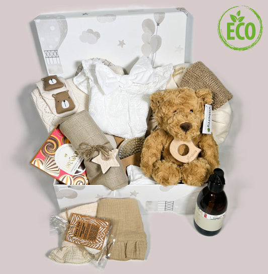 A baby girl hamper in a handmade baby keepsake box containing new mummy treats, cotton baby clothing, a teddy bear and neutral cotton baby blanket.