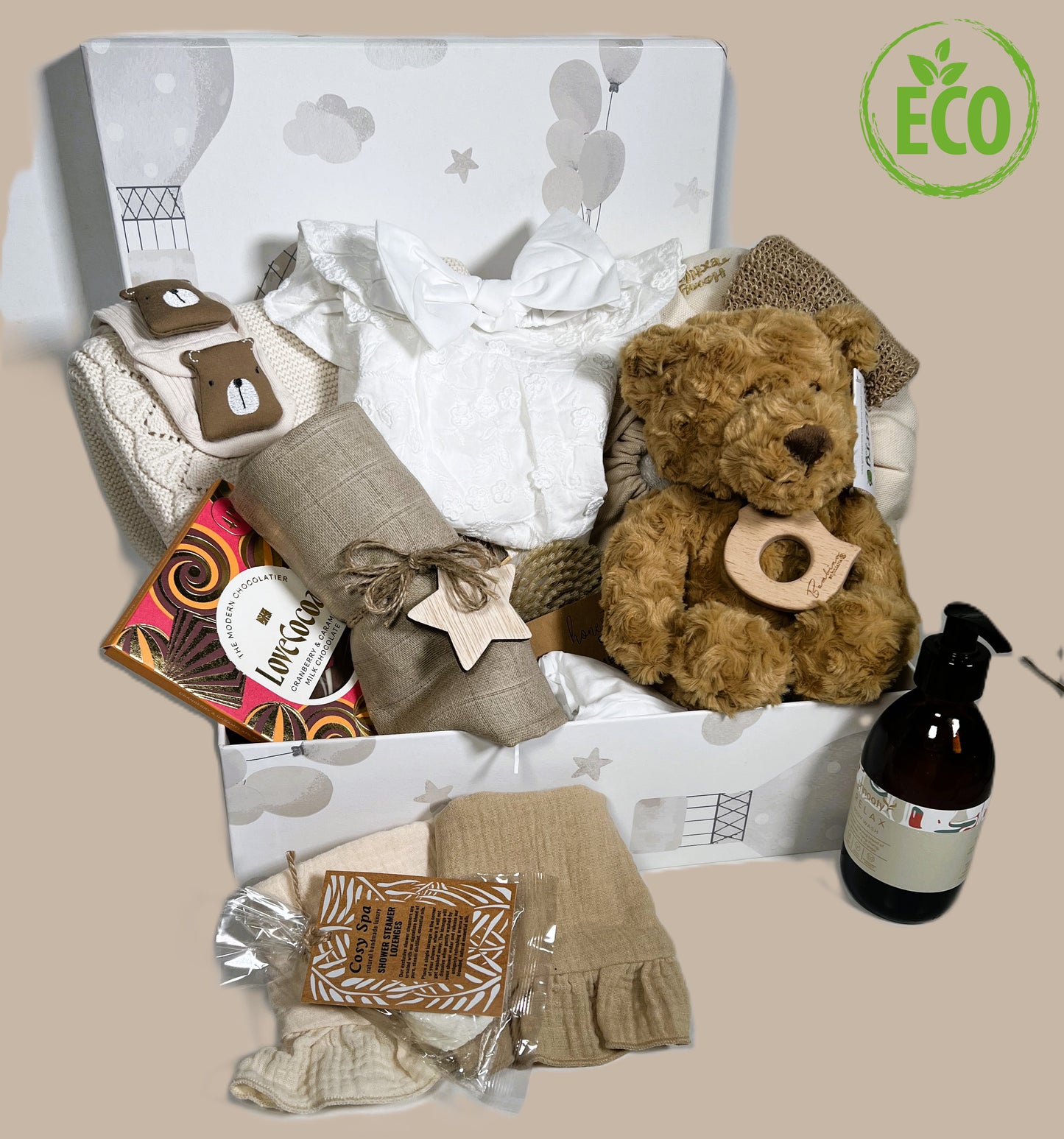 A baby girl hamper in a handmade baby keepsake box containing new mummy treats, cotton baby clothing, a teddy bear and neutral cotton baby blanket.