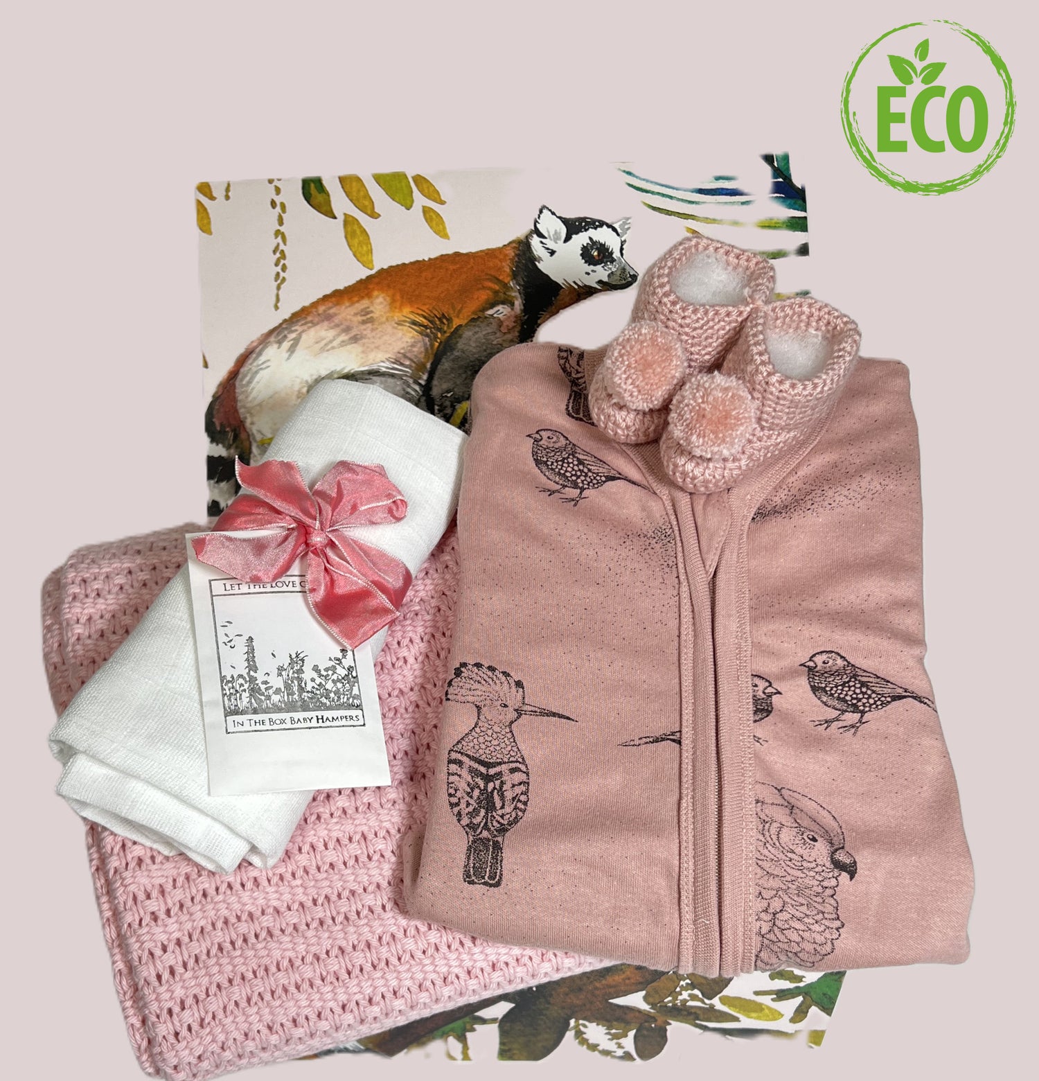 Grey cotton cellular baby blanket with a lovely dusky pink baby romper with exotic bird design, a muslin sqaure, a Choc Affair chocolate bar, a pair of crocheted baby booties with pompoms all in a handcrafted baby keepsake box with lima jungle print.