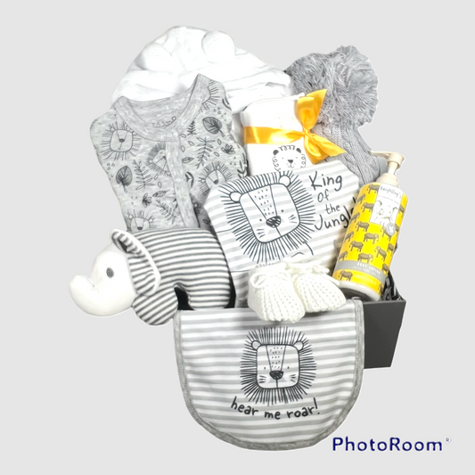 A baby boy gift hamper in a grey magnetic baby keepsake box containing 1 grey baby sleepsuit with a black print of lion faces and jungle leaves in black with a grey and white horizintally striped baby body suit with a picture of a lion and the words "King of the Jungle". There is amatching baby bib withe the words"hear me roar". A botle of vegan baby lotion, a white baby dressing gown, a white baby muslin with lion print, a grey baby pompom hat and a grey and white elephant baby rattle.