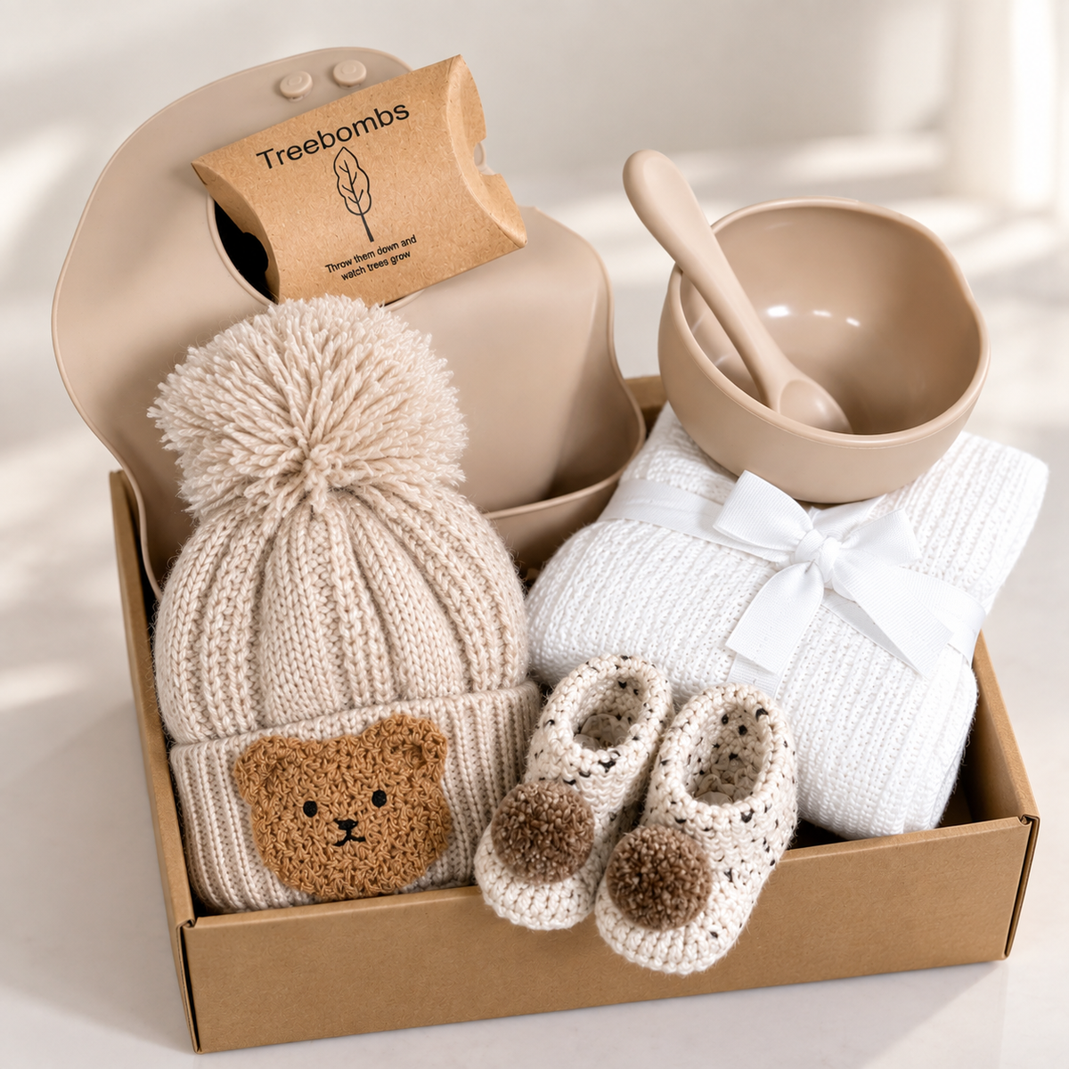 a neutral new baby gift with crocheted baby booties, a baby pompom hat with a bear badge, a silicone baby bib, feeding bowl and spoon and a white cotton cellular baby blanket.