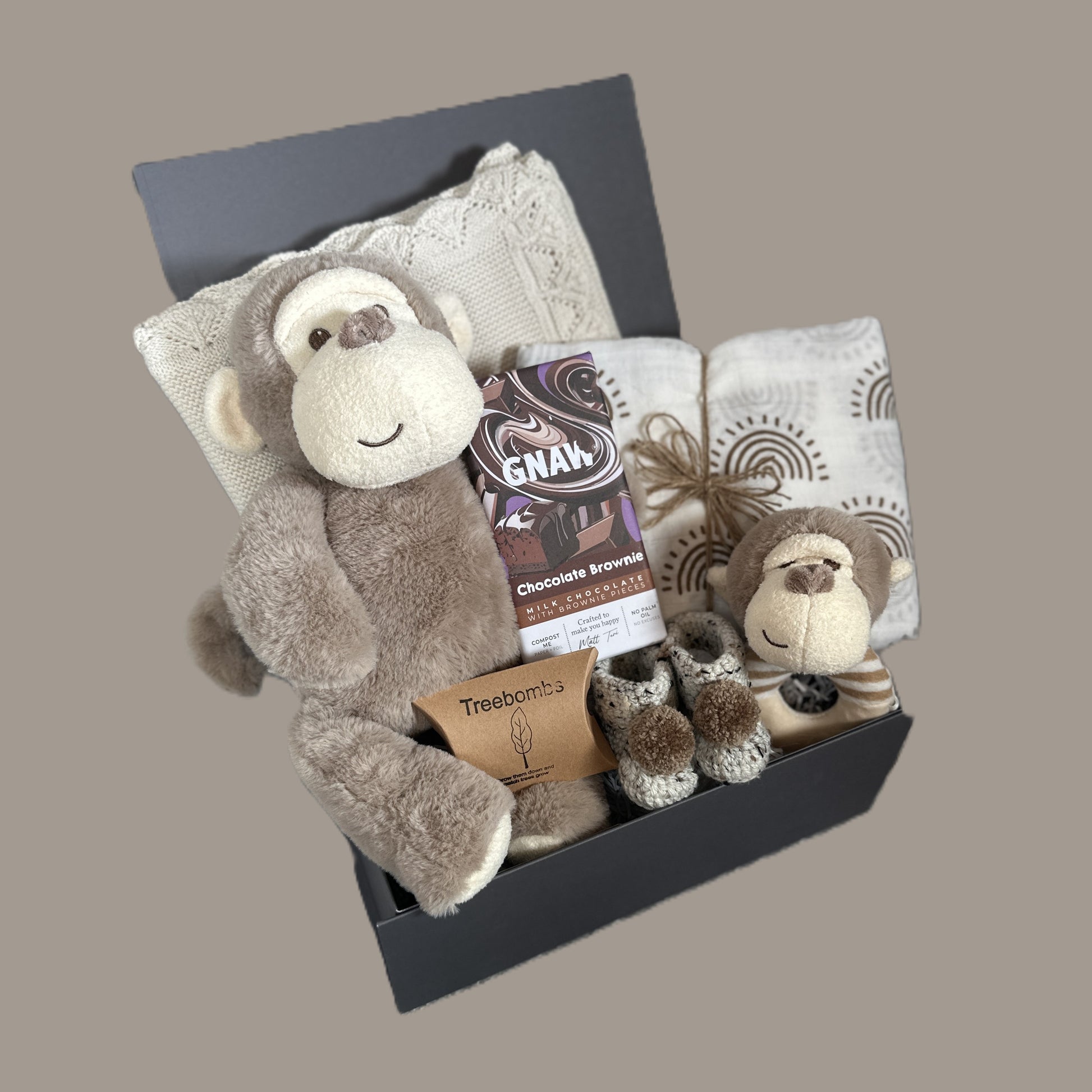 New Baby gift set with plush monkey, baby booties, a baby blanket  and swaddle on a gray background
