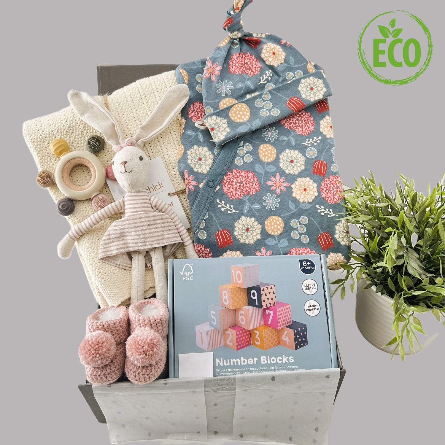 The eco friendly contents of this new baby girl gift are 1 x almond cotton cellular baby blanket, 1 x GOTS certified baby romper in blue cream and pink floral pateern with matching baby knot hat, a linen hare soft baby toy, a silicone teether a pair of baby booties in pink and a set of FSW wooden baby blocks.