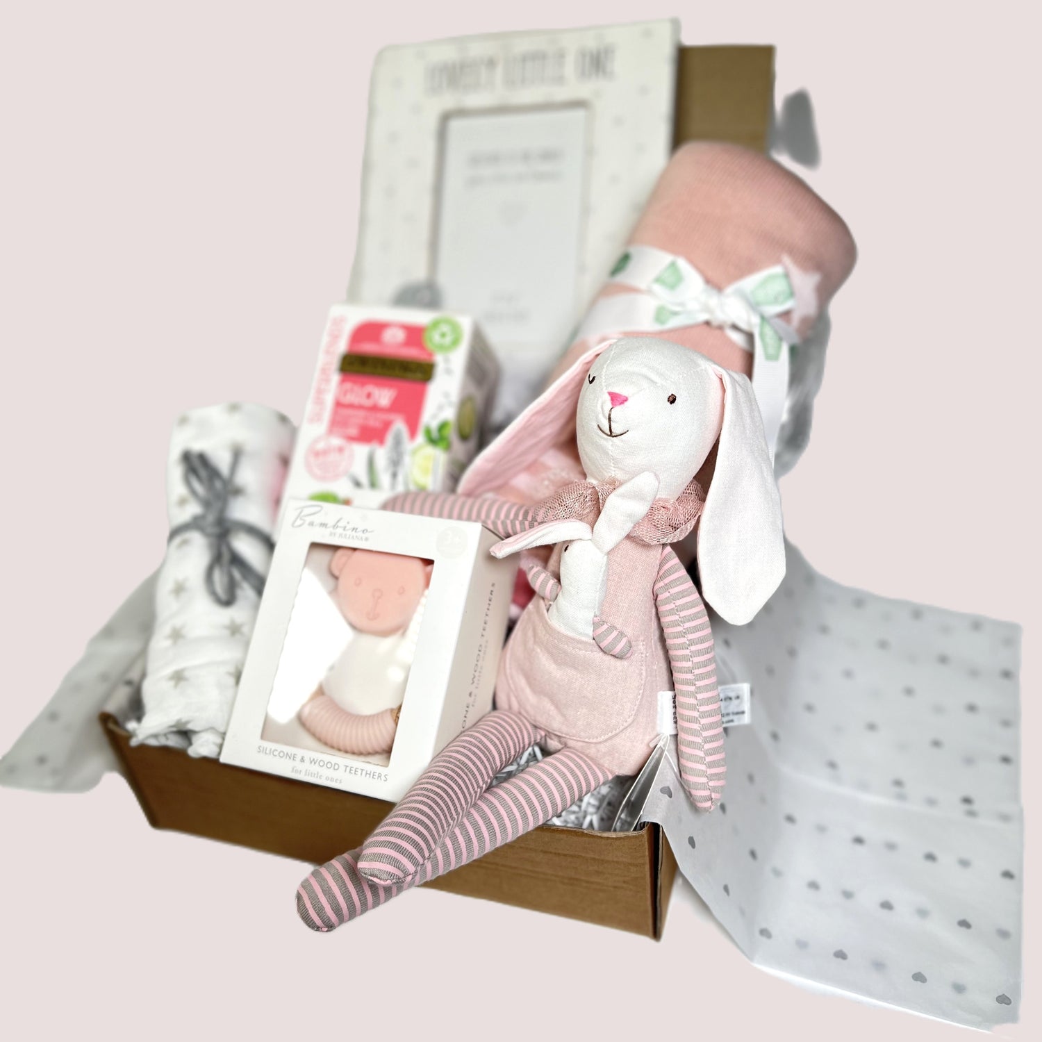 New parents gift hamper for a baby girl includes a pink star print cotton baby blanket, a bambino bear teether, a white and grey muslin square, a wooden photo frame and a packet of "Glow" teabags.