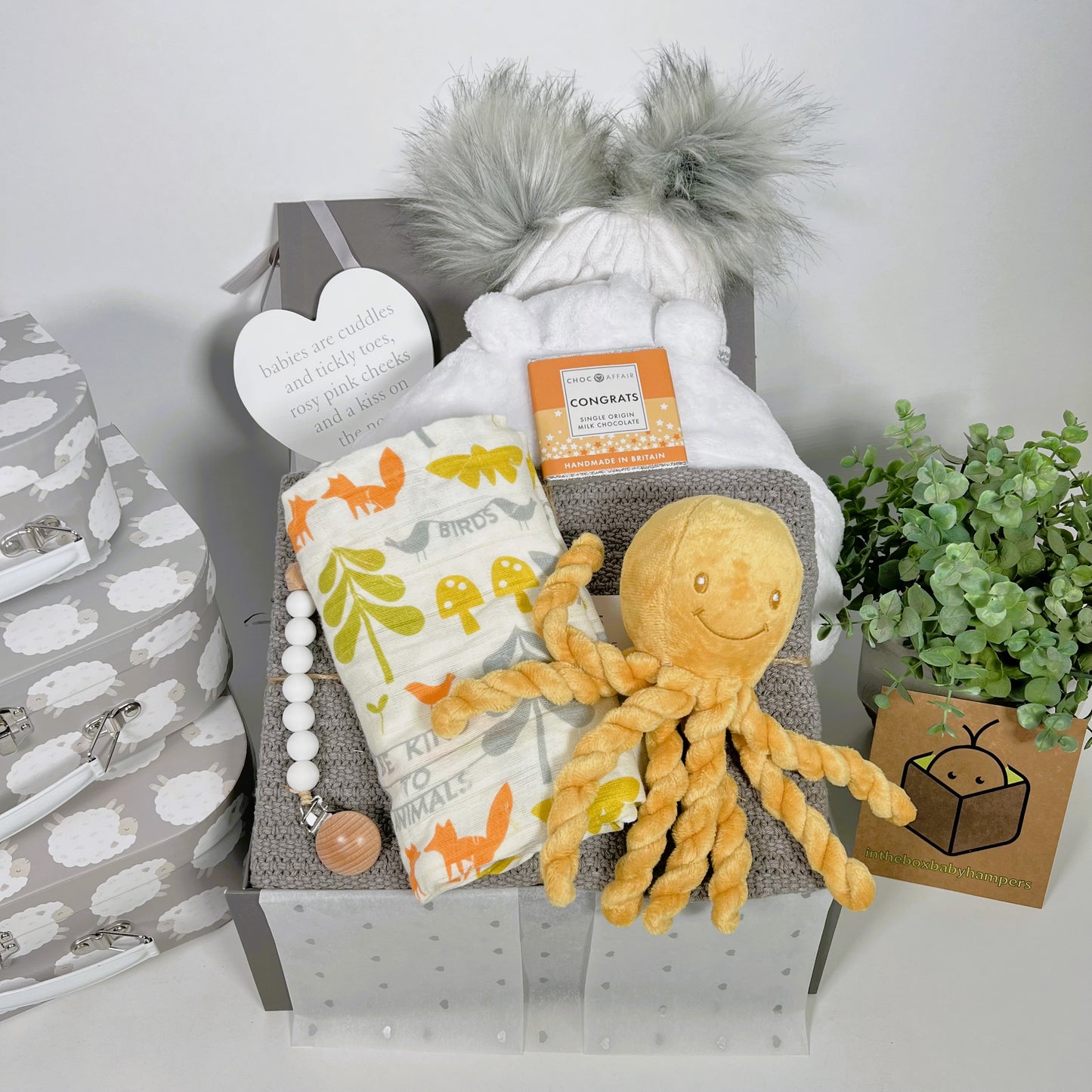 Luxury new baby hamper gift for the new parents containing a luxury cotton cellular baby blanket, a Pui Pui octopus soft baby toy, a white baby dressing gown, large muslin square, baby pompom hat, abar of chocolate , a nursery plaque and a dummy clip.