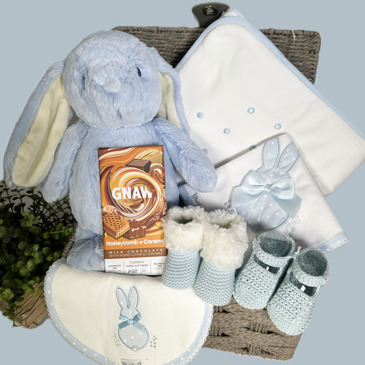A grey rope baby hamper with a Ebba blue bunny soft baby bunny, a white cotton hooded baby towel, matching bib and burp cloth and booties.
