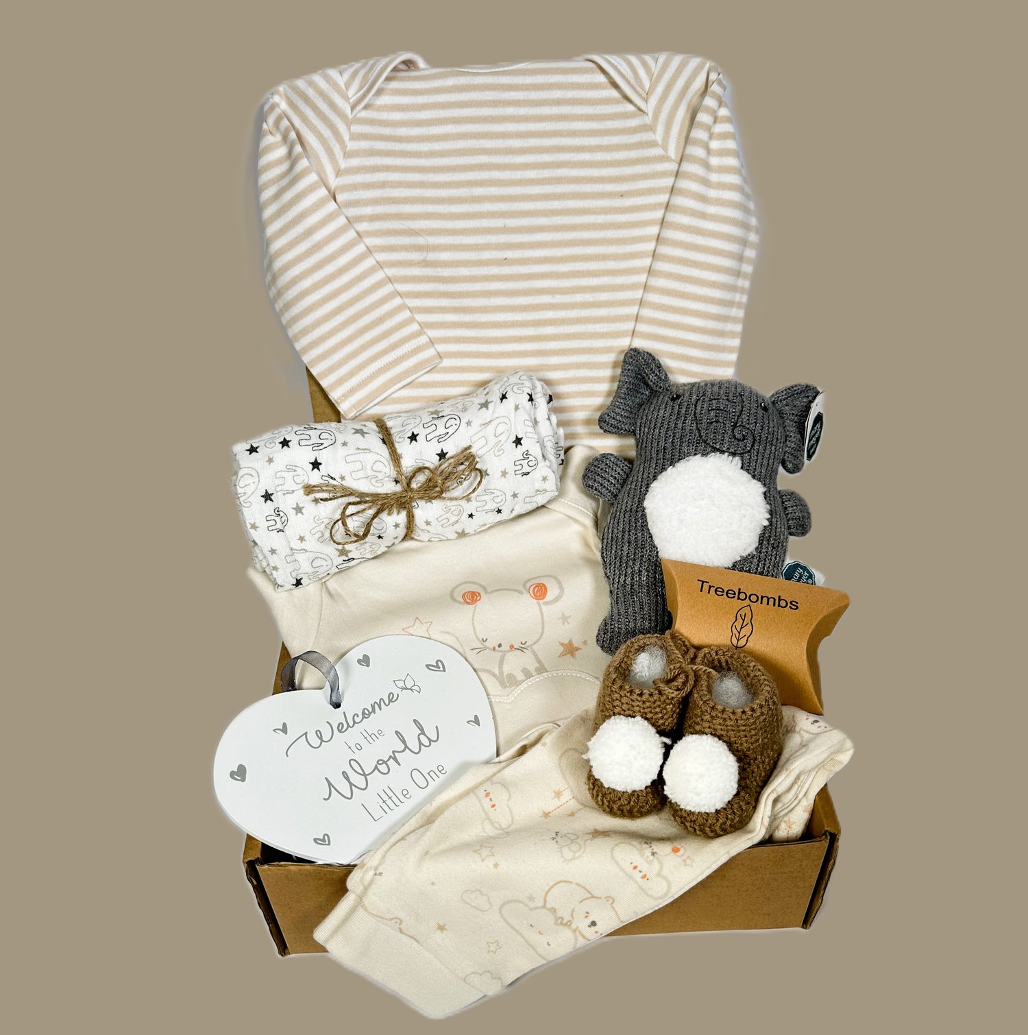 Elephant themed new mummy hamper containing  a Mary Meyer elephant baby rattle. A heart shaped nursery plaque. A pair of baby trousers and matching baby long sleeved t-shirt, a baby body suit.  matching band a pair of chrocheted baby booties with white pompoms.