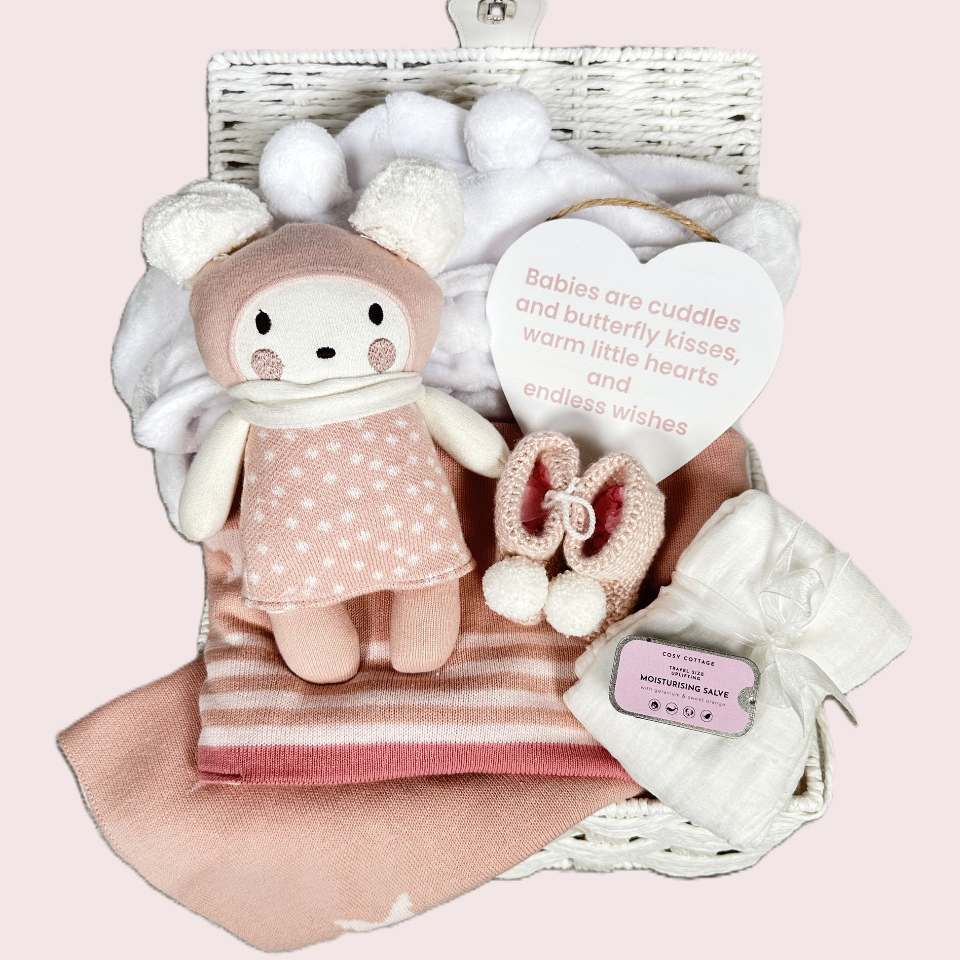 New baby girl gift hamper with plush toy, baby blanket, and baby items on a pink background