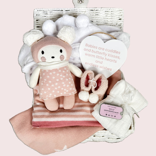 New baby girl gift hamper with plush toy, baby blanket, and baby items on a pink background