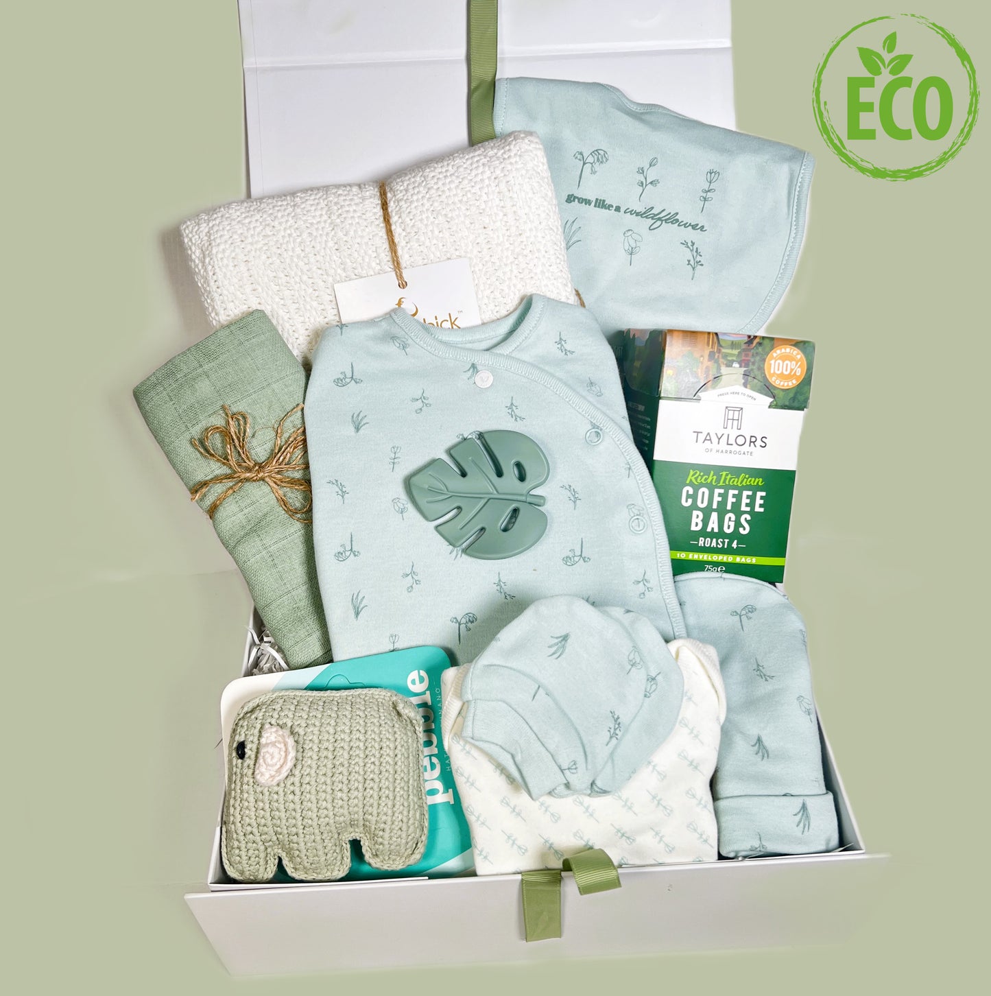 A newborn baby girl hamper gift in "hello Baby" baby keepsake box containing a 6 piece organci cotton baby layette set in mint green with a darker green pencil drawing design of wildflowers. The baby bib reads "Grow like a wildflower". Alos included is a green food garde silicone baby teether shaped like a leaf, a Pebblechild hand crafted elephant baby rattle, a whicte |Hippychick cellular baby blanket, a green muslin square and a pack of Taylors coffee bags.