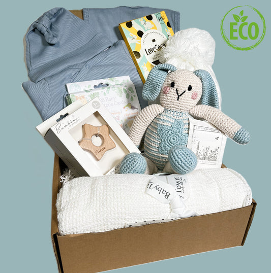 New baby boy gift includes a blue baby sleepsuit with fold over cuffs and a matching baby knot hat and baby bib in a denim blue colour, a white cotton cellular baby blanket, a bar of Love Cocoa chocolate, and a blue crochet bunny from Pebblechild.