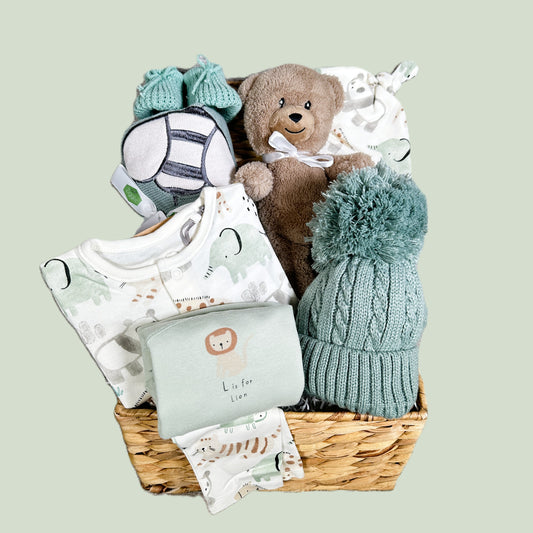 Baby gift basket with teddy bear, knitted hat, and clothes on a light green background