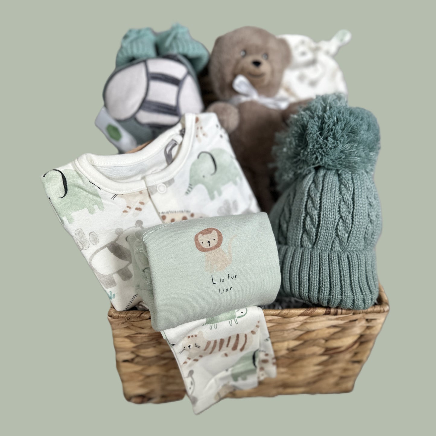 Baby gift basket with clothes, a hat, and a teddy bear on a light gray background