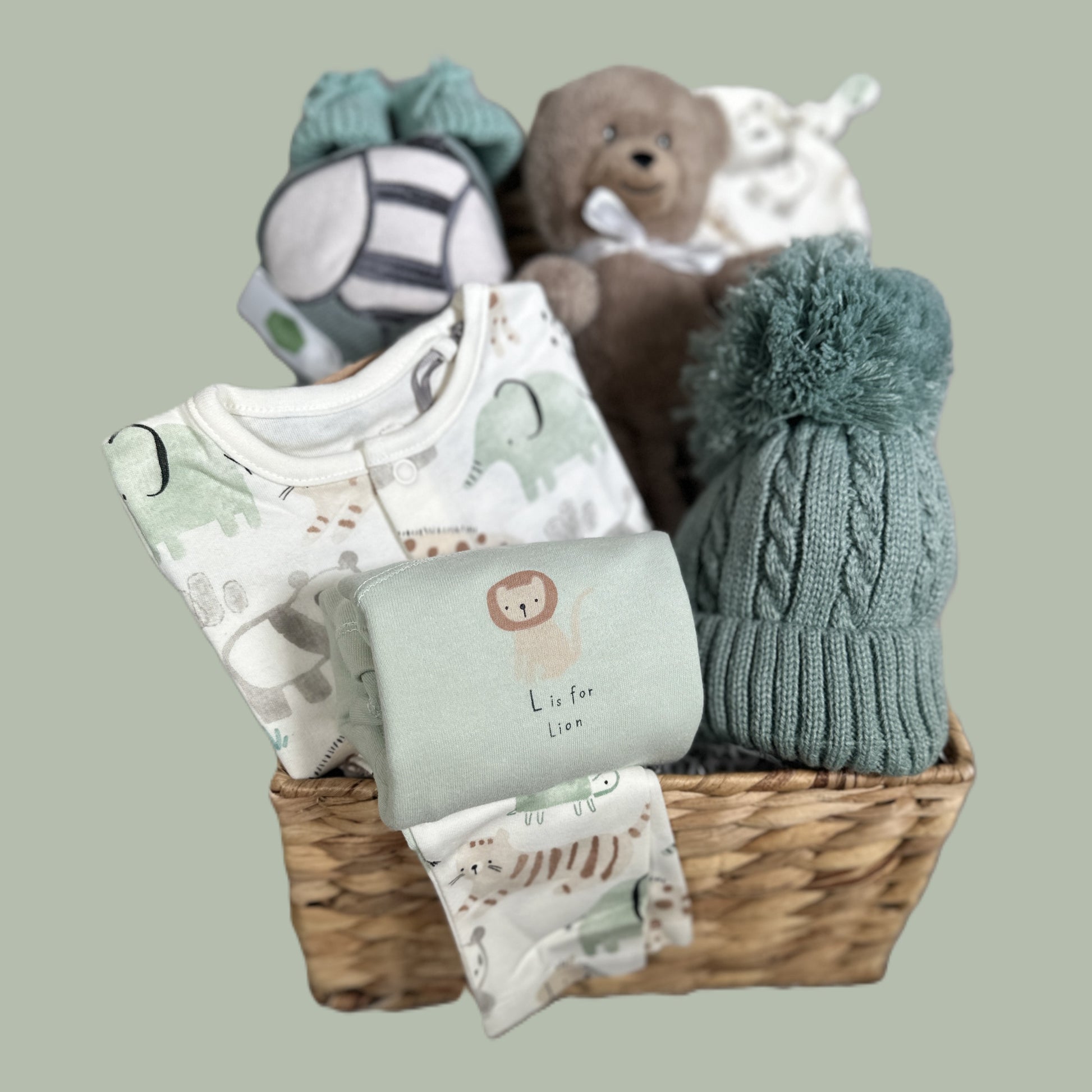 Baby gift basket with clothes, a hat, and a teddy bear on a light gray background