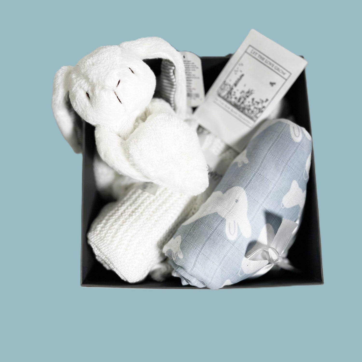 A baby boy hamper gift in  baby keepsake box containing A blue and white bunny print muslin swaddle blanket, a Mary Meyer bunny baby comforter, a white cellular baby blanket, a FSC wooden baby rattle and a nursery decoration.