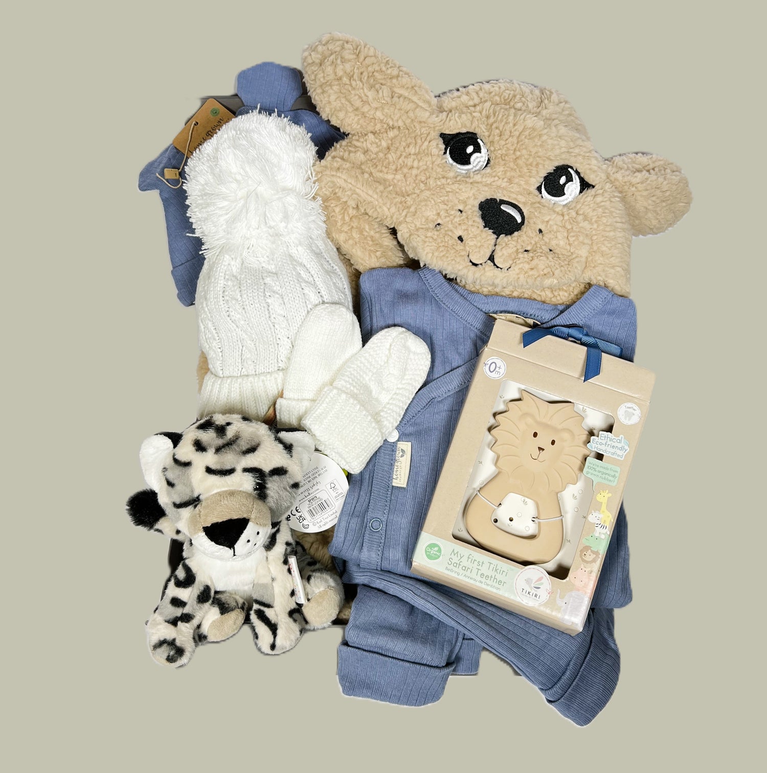 A new baby hamper with a puppy baby dressing gown, Tikiri lion baby teether, blue organic baby layette set, white baby pompom hat and matching mittens and a Pippins snow leopard soft baby toy.