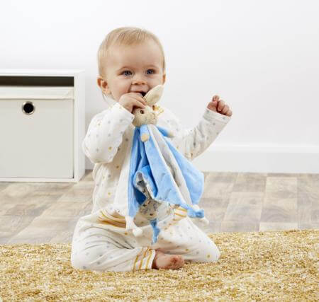 Baby Sitting on the floor with a Peter Rabbit comforter blanket.