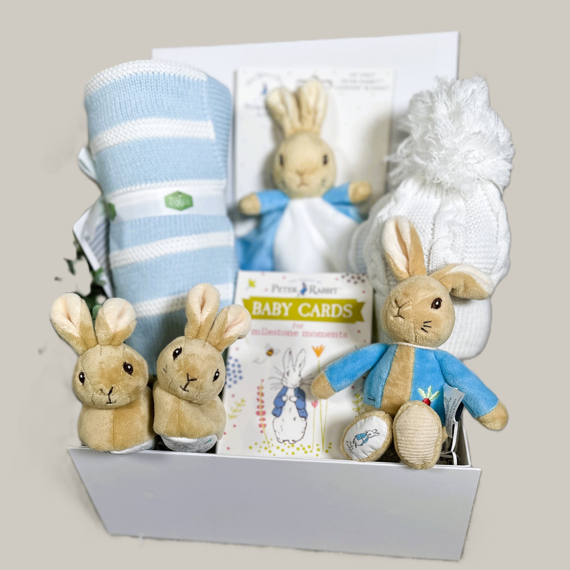 Baby gift hamper with peter Rabbit plush toys and baby items on a light pale background