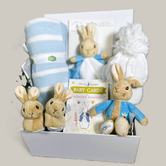 Baby gift hamper with peter Rabbit plush toys and baby items on a light pale background