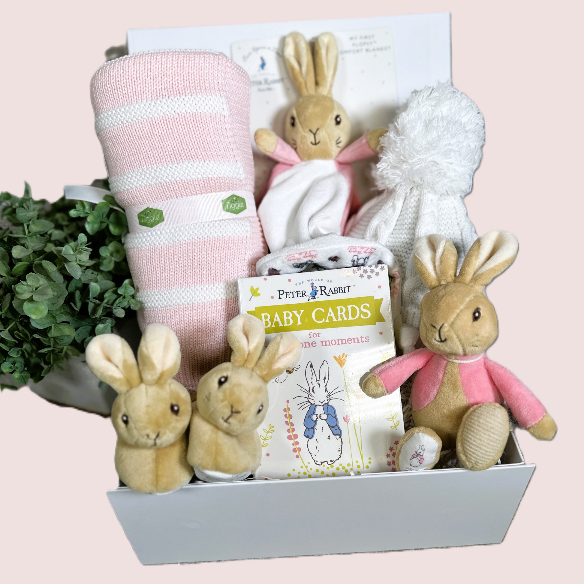 Baby gift hamper with Flopsey bunny  plush toys, blanket, and baby cards on a light pink background