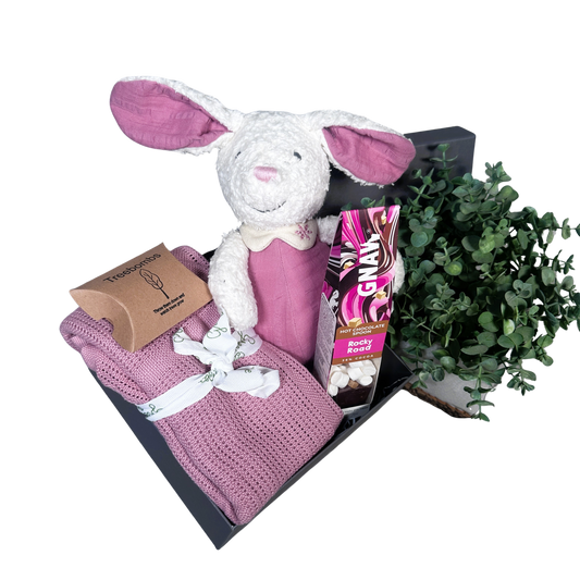 pink baby girl hamper with bunny soft toy, baby blanket and hot chocolate stirrer.