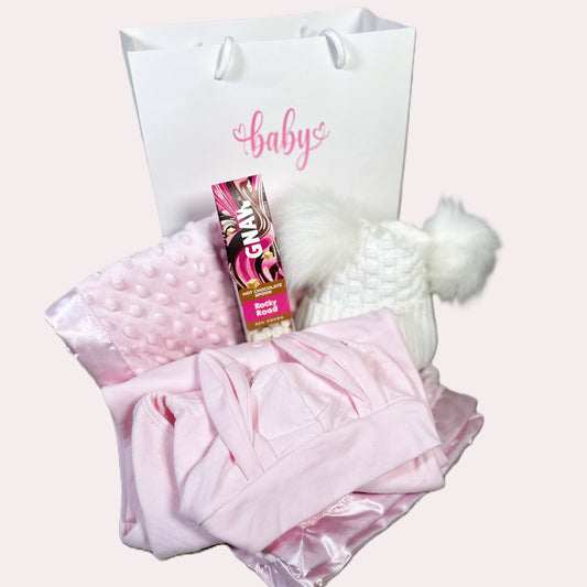 Baby gift with pink blanket, hat, and product on a Gnaw rocky road hot chocolate stirrer white background.