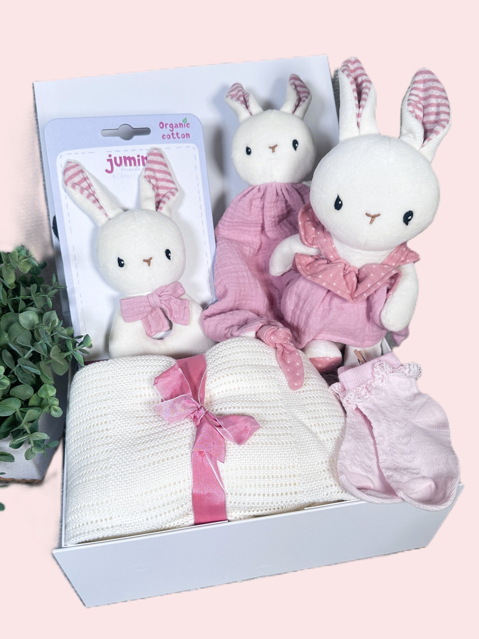 Baby gift set with plush bunnies, blanket, and booties in a box on a pink background