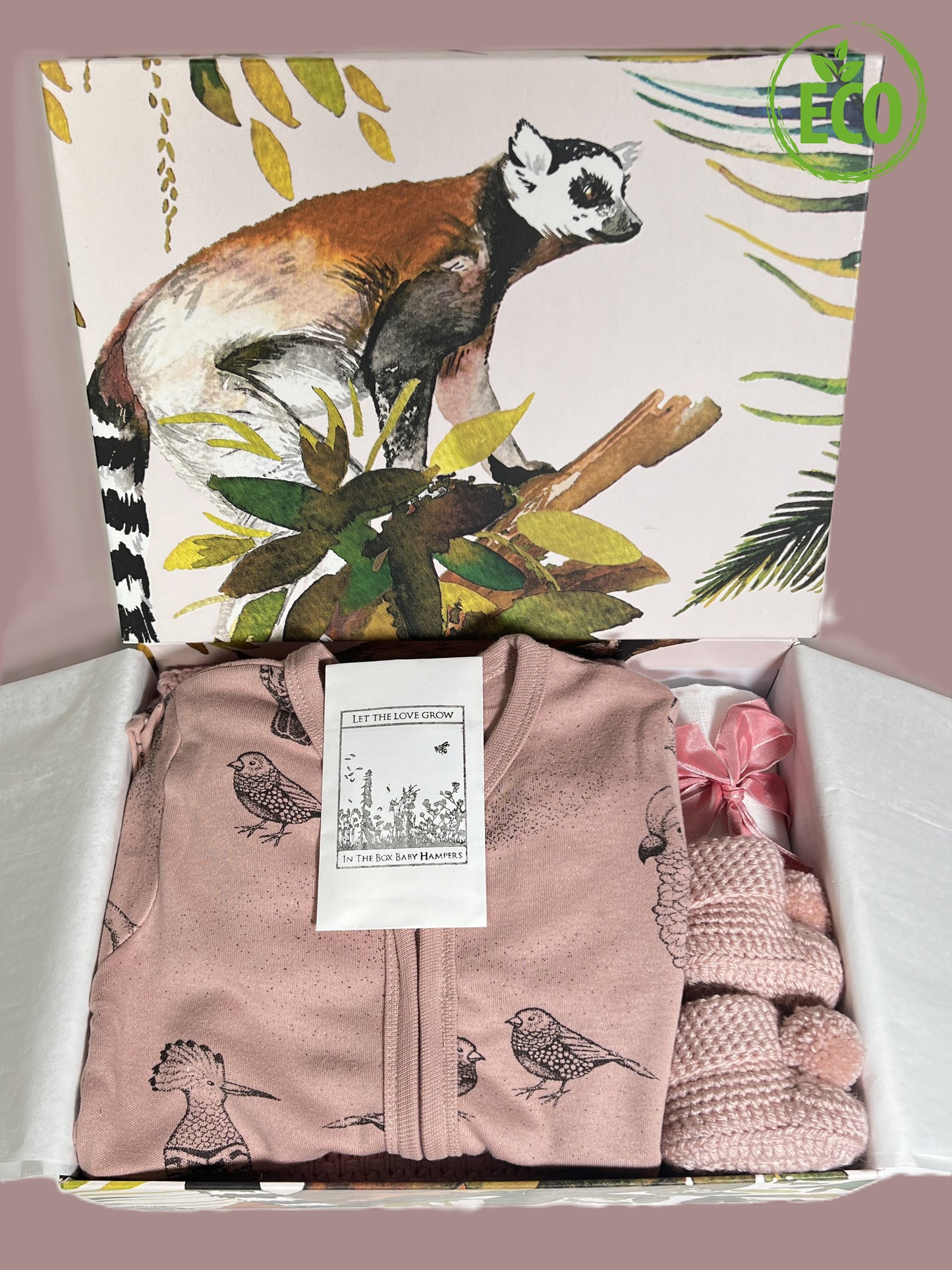 Grey cotton cellular baby blanket with a lovely dusky pink baby romper with exotic bird design, a muslin sqaure, a Choc Affair chocolate bar, a pair of crocheted baby booties with pompoms all in a handcrafted baby keepsake box with lima jungle print.