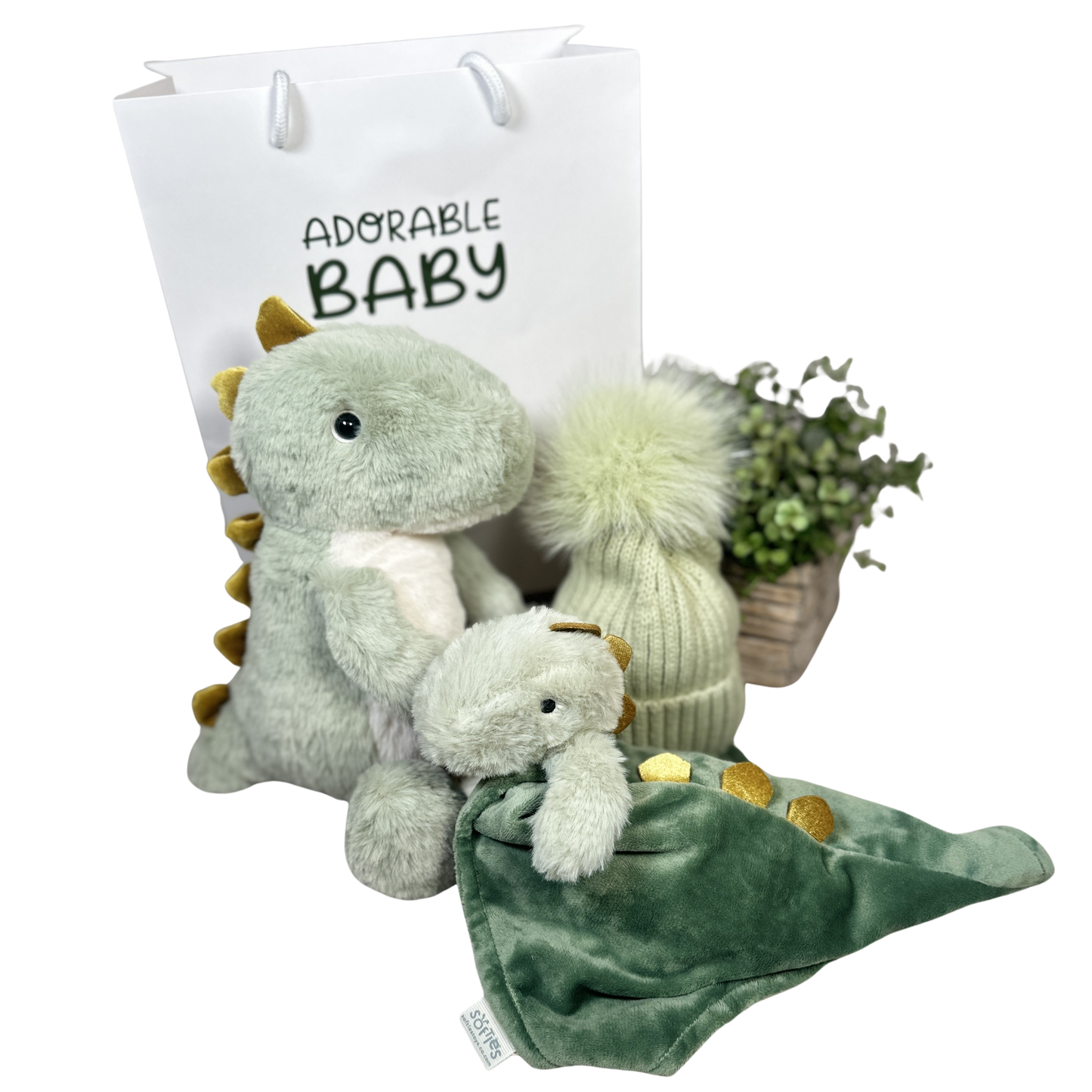 Baby gift set with plush dinosaur, hat, and blanket in front of a 'Adorable Baby' bag.