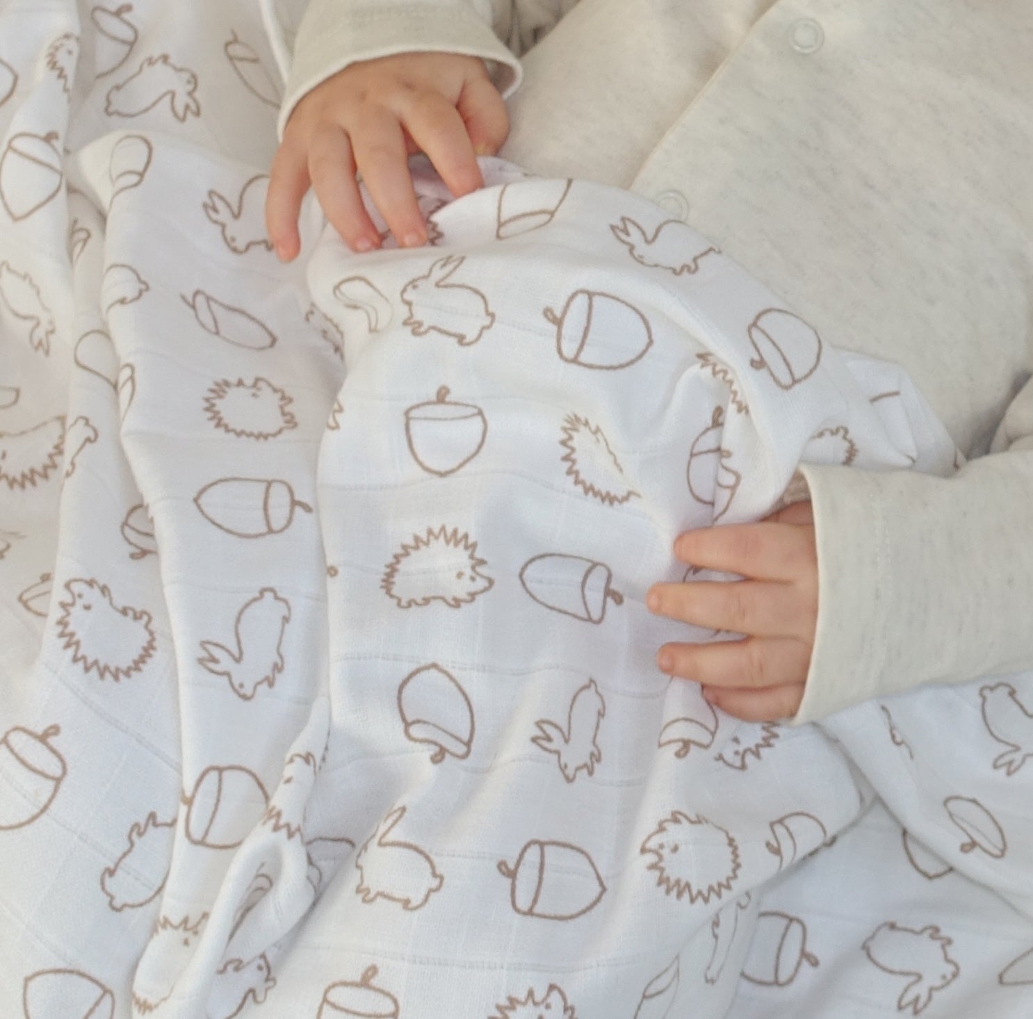 baby and muslin square with hedgehog and acorn pattern