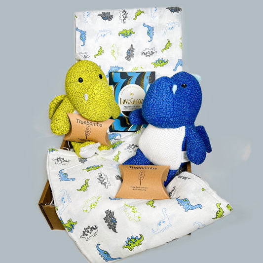 Twin boys baby gift hamper containing two Wilberry knitted dragon soft baby toys, 1 is blue the other is green, 2 large muslins with a dinosaur print in blue white and green, 2 packets of Treebombs and a bar of Love Cocoa chocolate.