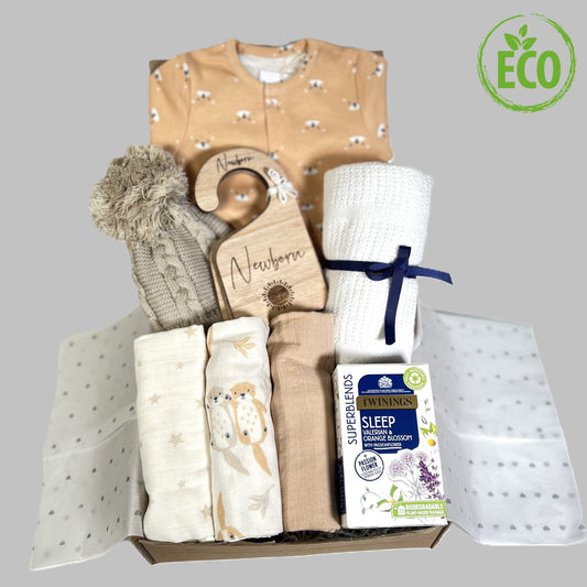 a baby shower gift of a neutral new baby hamper filled with organic cotton new baby essentials including a otter print sleepsuit and a set of three muslin squares.