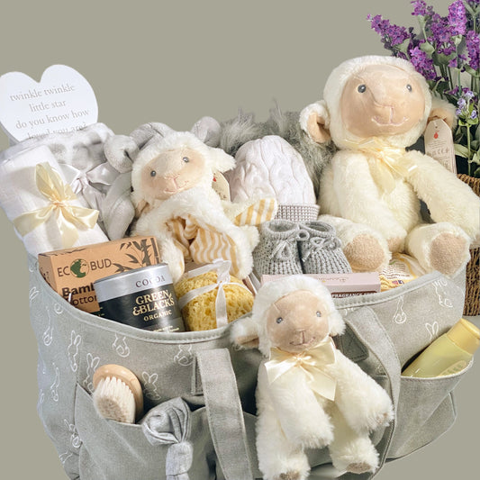 This nappy caddy baby gift hamper comes in a grey and white nappy caddy with a white bunny print and contains 3 Keeleco lamb baby toys, a grey and white baby soft blanket, a white muslin square, a pair of baby booties, a can of Green and Blacks drinking chocolate, a baby wooden hairbrush, a baby knot hat, a baby pom pom hat, a baby sponge, a grey hooded baby dressing gown, a pack of Kit and Kin nappies, a bottle of paraben free baby wash.