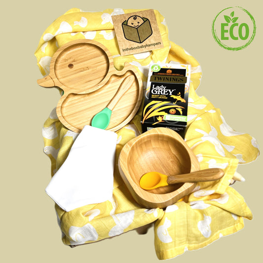 Baby weaning gift with a bamboo duck shaped plate and a bamboo bowl both with silicone and bamboo baby spoons, a large yellow and white bamboo baby muslin and a packet of Earl grey Twinings teabags