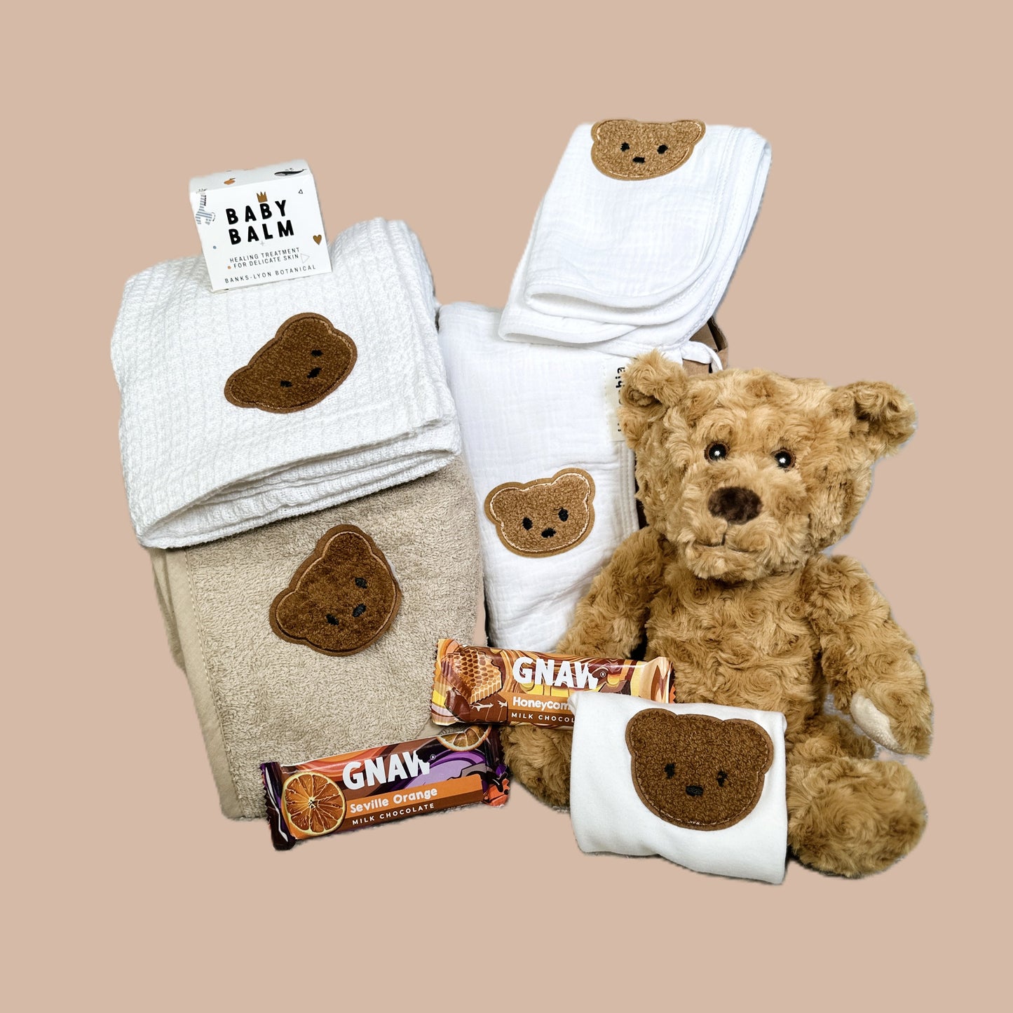 Baby gift set with teddy bear, towels, and snacks on a beige background