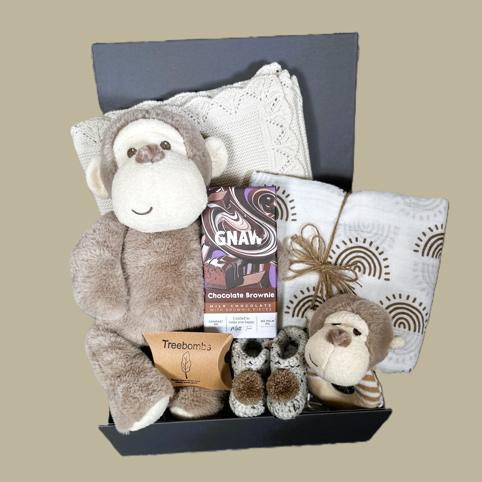 New baby hamper with plush monkey, chocolate brownie chocolate bar, and other items on a beige background